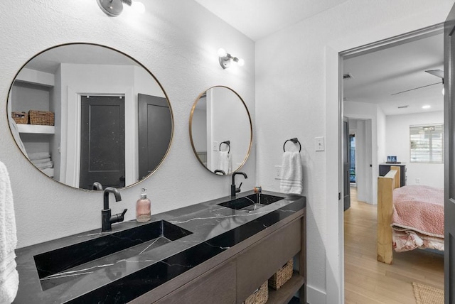 full bath with ensuite bath, double vanity, wood finished floors, and a sink