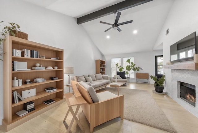 living room featuring beamed ceiling, high vaulted ceiling, a ceiling fan, light wood-style floors, and a lit fireplace