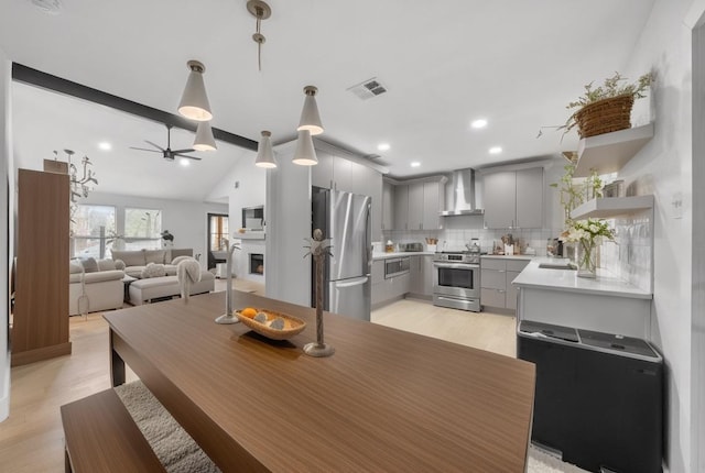 dining space featuring light wood finished floors, visible vents, vaulted ceiling with beams, a lit fireplace, and a ceiling fan