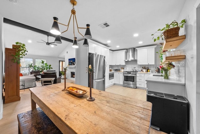 dining area with visible vents, a warm lit fireplace, light wood-style flooring, and a ceiling fan