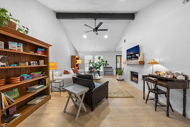 living room featuring beam ceiling, light wood-style flooring, a ceiling fan, and a lit fireplace