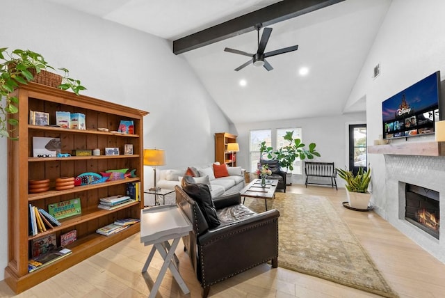 living room with beam ceiling, wood finished floors, a warm lit fireplace, and high vaulted ceiling