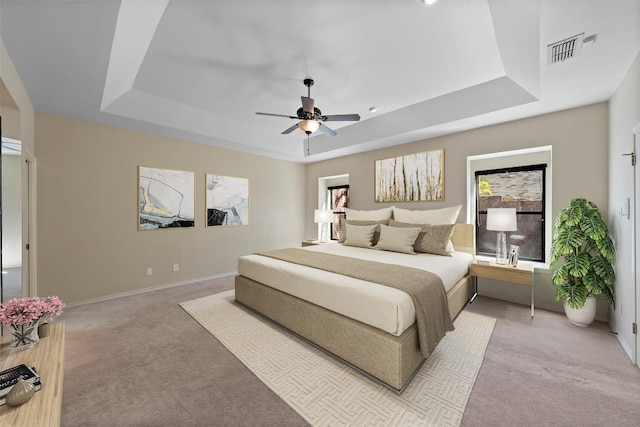 carpeted bedroom featuring a ceiling fan, a raised ceiling, baseboards, and visible vents