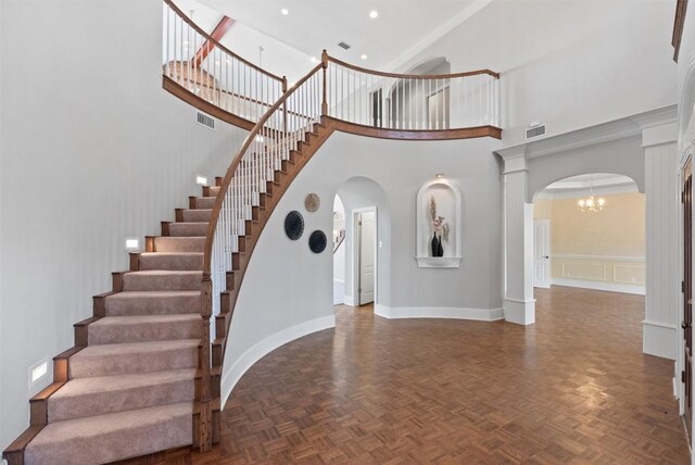 stairway with a high ceiling, a notable chandelier, visible vents, and arched walkways