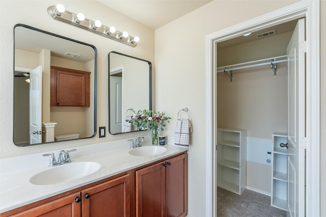 full bathroom with double vanity, a spacious closet, visible vents, and a sink