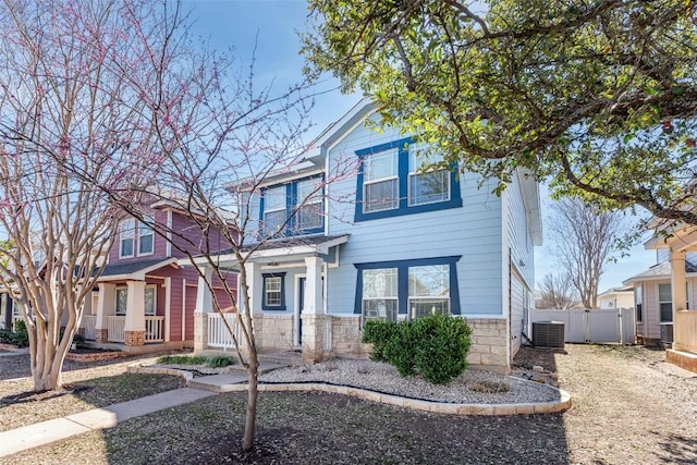 view of front of house featuring stone siding, covered porch, central air condition unit, and fence