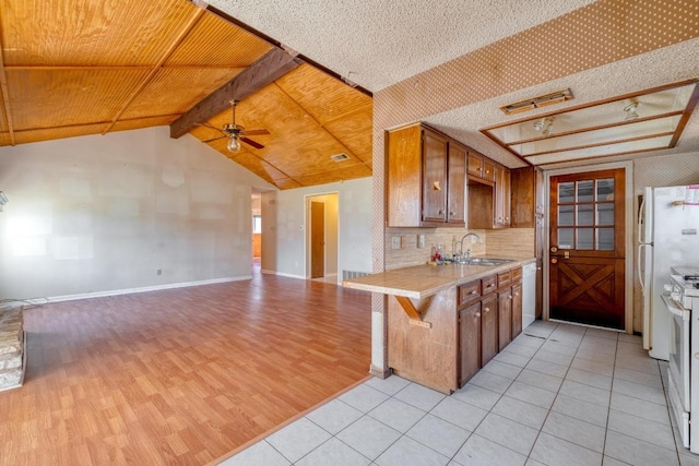 kitchen with lofted ceiling with beams, light countertops, brown cabinets, a ceiling fan, and a sink