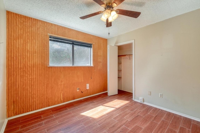 unfurnished bedroom featuring a ceiling fan, a textured ceiling, a closet, wooden walls, and wood tiled floor