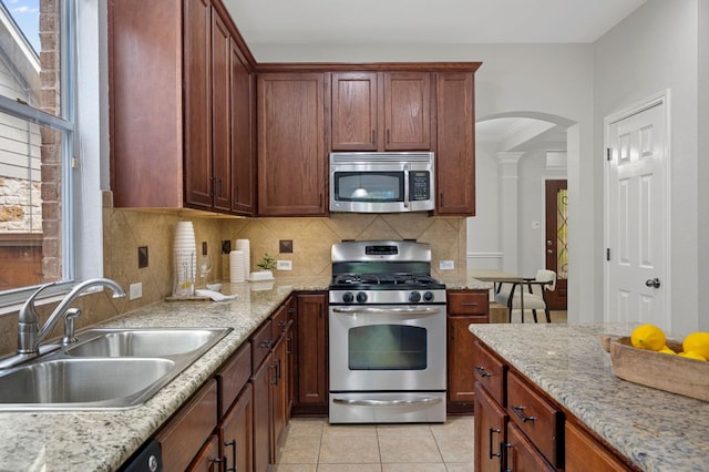 kitchen featuring backsplash, light tile patterned floors, arched walkways, stainless steel appliances, and a sink