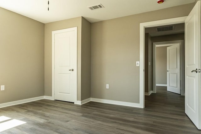 unfurnished bedroom with dark wood-style floors, visible vents, and baseboards