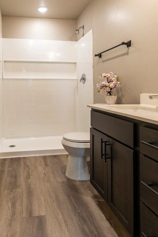 bathroom with a shower stall, toilet, vanity, and wood finished floors