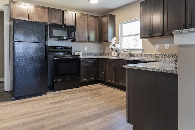 kitchen with dark brown cabinetry, black appliances, light wood-type flooring, and a sink