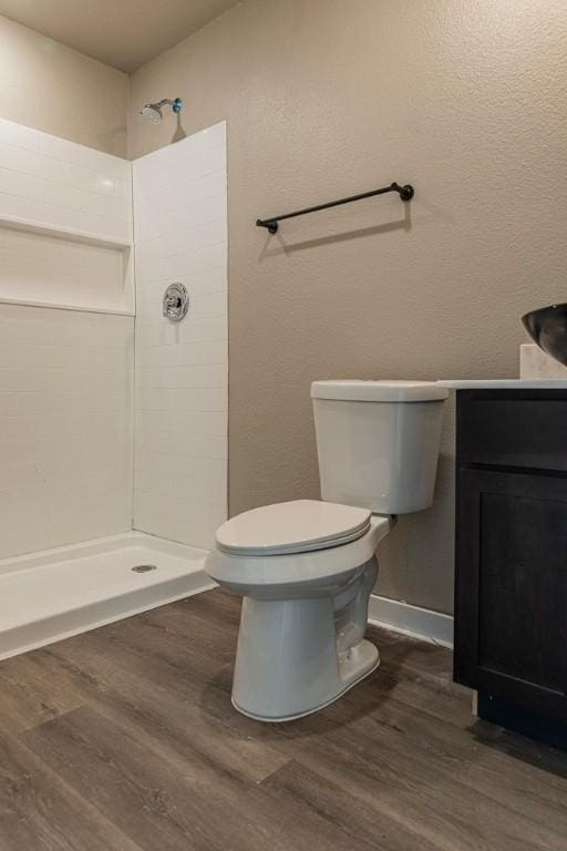 full bath featuring toilet, wood finished floors, vanity, and a tile shower