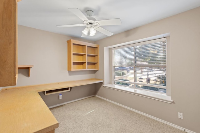 unfurnished office featuring baseboards, built in desk, carpet flooring, and a ceiling fan