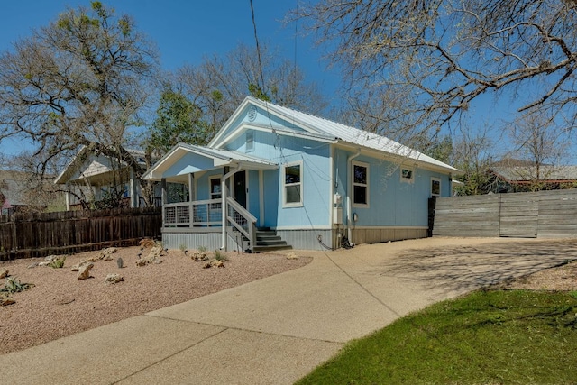 view of front of home with metal roof, a porch, driveway, and fence