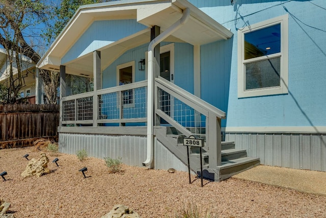 view of side of home featuring stairway, covered porch, and fence