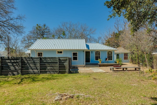 rear view of property with a lawn, metal roof, and fence