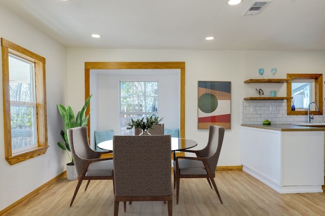 dining room featuring light wood finished floors, visible vents, a healthy amount of sunlight, and baseboards