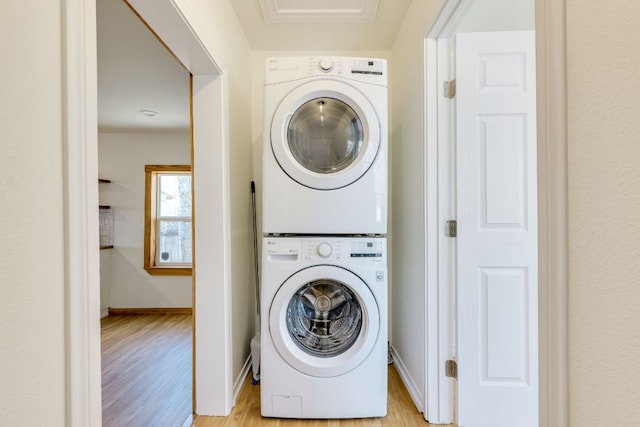 laundry room featuring laundry area, stacked washer / dryer, baseboards, and light wood-type flooring