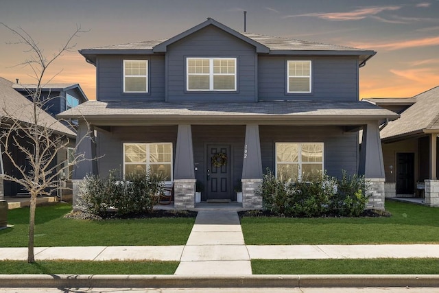 craftsman-style home with stone siding, a lawn, and a porch