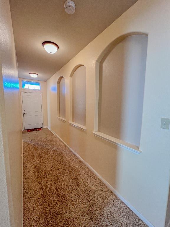 corridor featuring baseboards, light carpet, and light tile patterned flooring