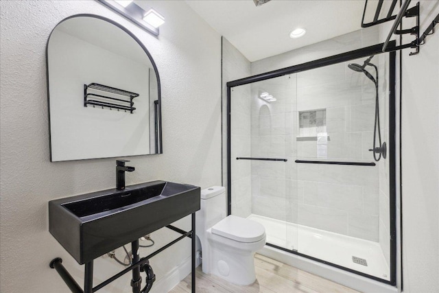 bathroom featuring a stall shower, toilet, a textured wall, and wood finished floors