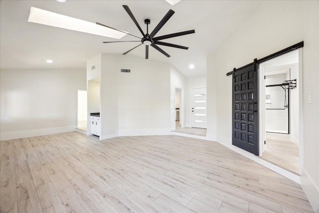 empty room featuring a barn door, a ceiling fan, light wood finished floors, and lofted ceiling with skylight