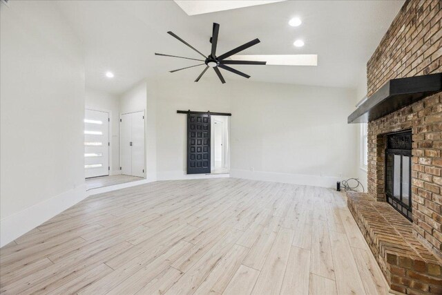 unfurnished living room with a ceiling fan, wood finished floors, a barn door, a fireplace, and baseboards