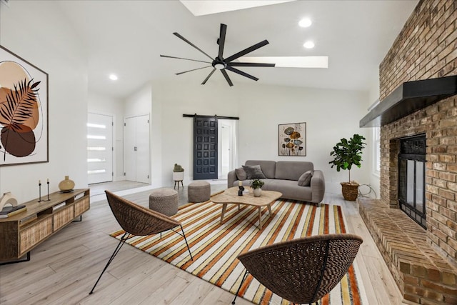 living area featuring light wood-type flooring, a barn door, a fireplace, high vaulted ceiling, and a ceiling fan