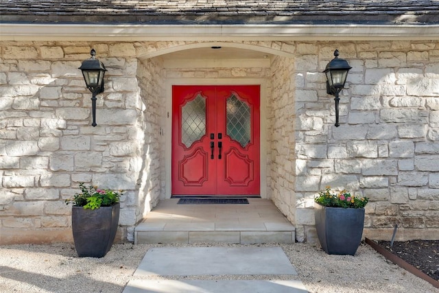 doorway to property featuring stone siding and a shingled roof