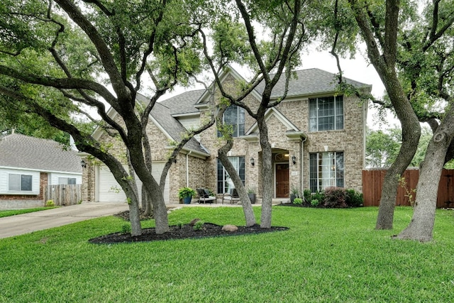 traditional-style home with fence, roof with shingles, concrete driveway, a front lawn, and brick siding