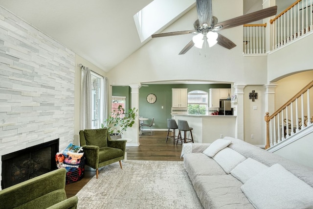 living area with a stone fireplace, decorative columns, wood finished floors, and ceiling fan