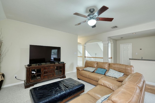 carpeted living area with visible vents, ceiling fan, baseboards, and decorative columns