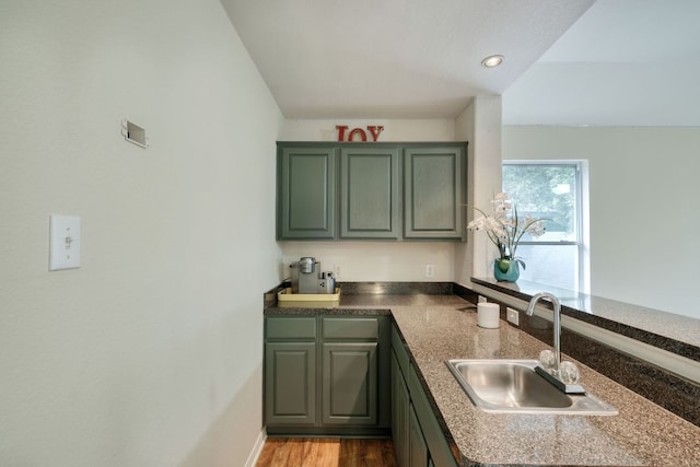 kitchen with wood finished floors, a peninsula, recessed lighting, a sink, and green cabinets