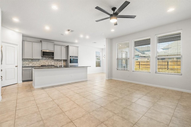 kitchen featuring gray cabinets, dark countertops, open floor plan, appliances with stainless steel finishes, and decorative backsplash