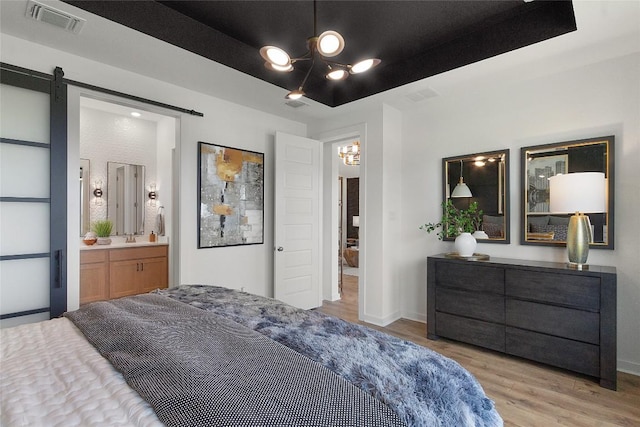 bedroom featuring a barn door, visible vents, wood finished floors, and a chandelier