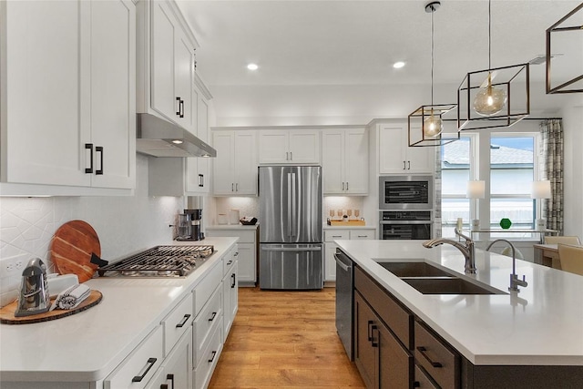 kitchen featuring light wood-style flooring, under cabinet range hood, a sink, appliances with stainless steel finishes, and light countertops