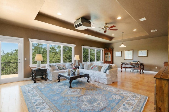 living room with visible vents, a raised ceiling, baseboards, and light wood-style flooring