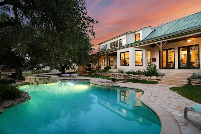 pool at dusk featuring a pool with connected hot tub and a patio area