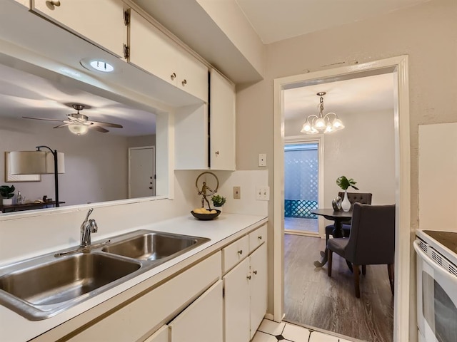 kitchen with a sink, ceiling fan with notable chandelier, light countertops, and white cabinetry