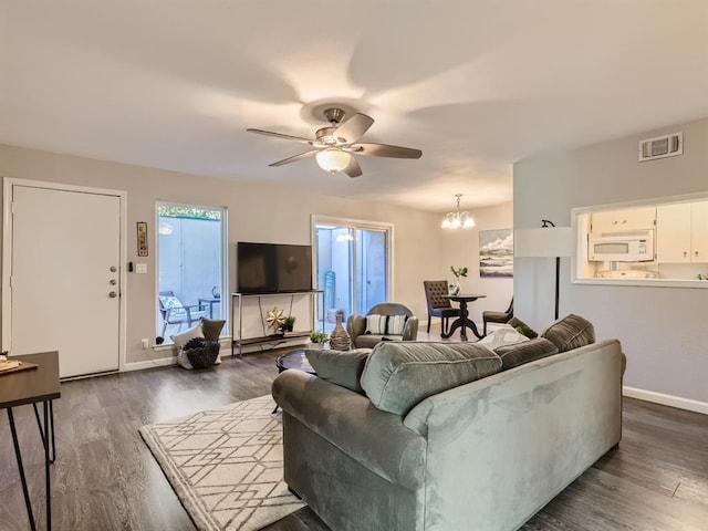 living area with visible vents, baseboards, dark wood finished floors, and ceiling fan with notable chandelier