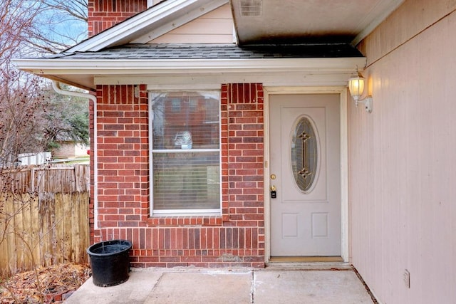 doorway to property featuring fence, brick siding, roof with shingles, and a chimney