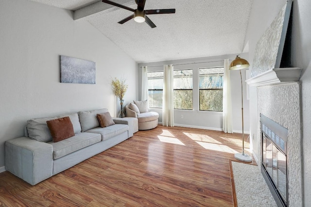 living area featuring a ceiling fan, a textured ceiling, wood finished floors, a fireplace, and vaulted ceiling with beams