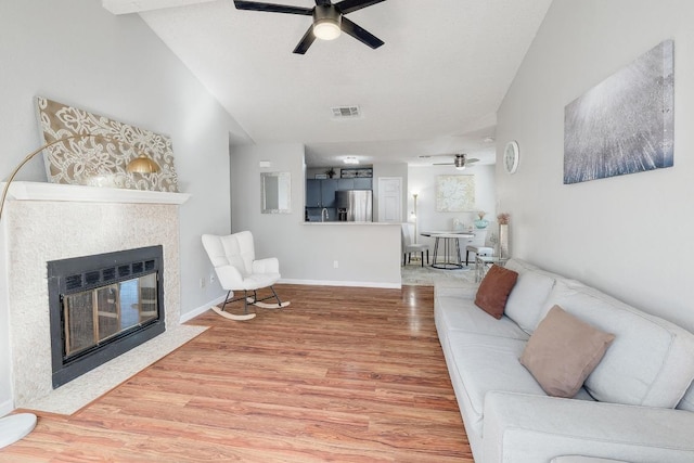 living room with visible vents, ceiling fan, a fireplace with flush hearth, vaulted ceiling, and wood finished floors