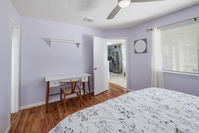 bedroom featuring visible vents, wood finished floors, stainless steel fridge, a textured ceiling, and a ceiling fan