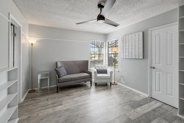 living area with ceiling fan, wood finished floors, baseboards, and a textured ceiling