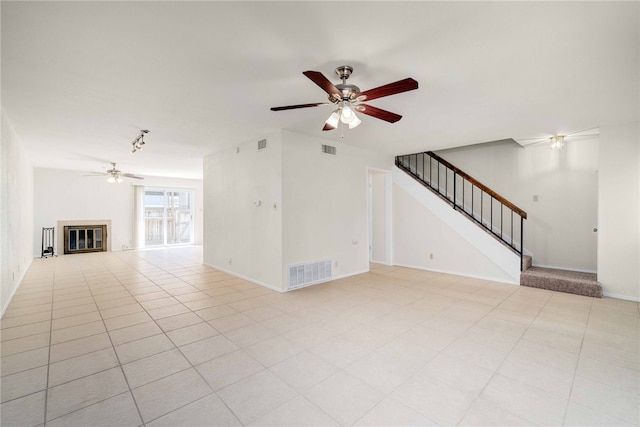 unfurnished living room featuring stairs, a glass covered fireplace, a ceiling fan, and visible vents