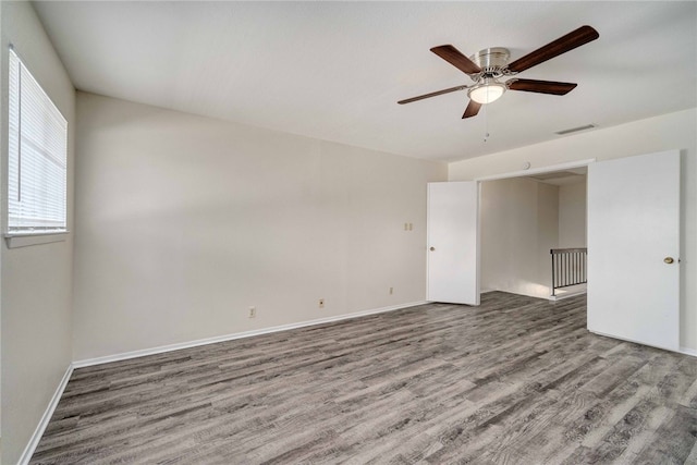 empty room featuring a ceiling fan, wood finished floors, visible vents, and baseboards