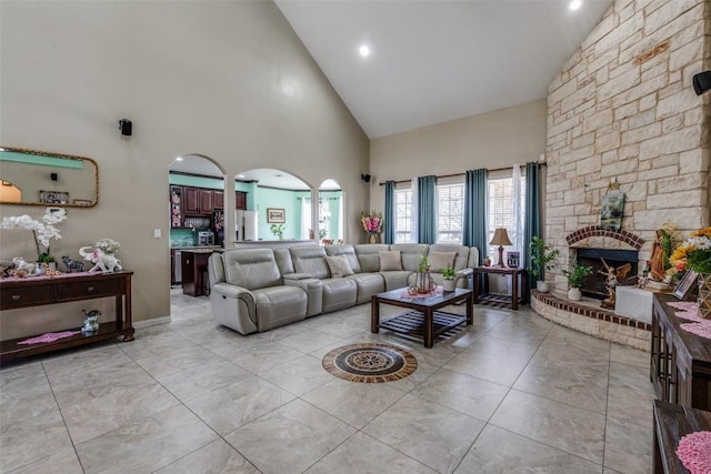 living room with a stone fireplace, arched walkways, and high vaulted ceiling