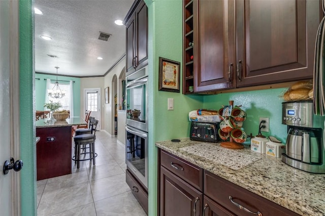 kitchen featuring a breakfast bar, dark brown cabinets, visible vents, and a textured ceiling